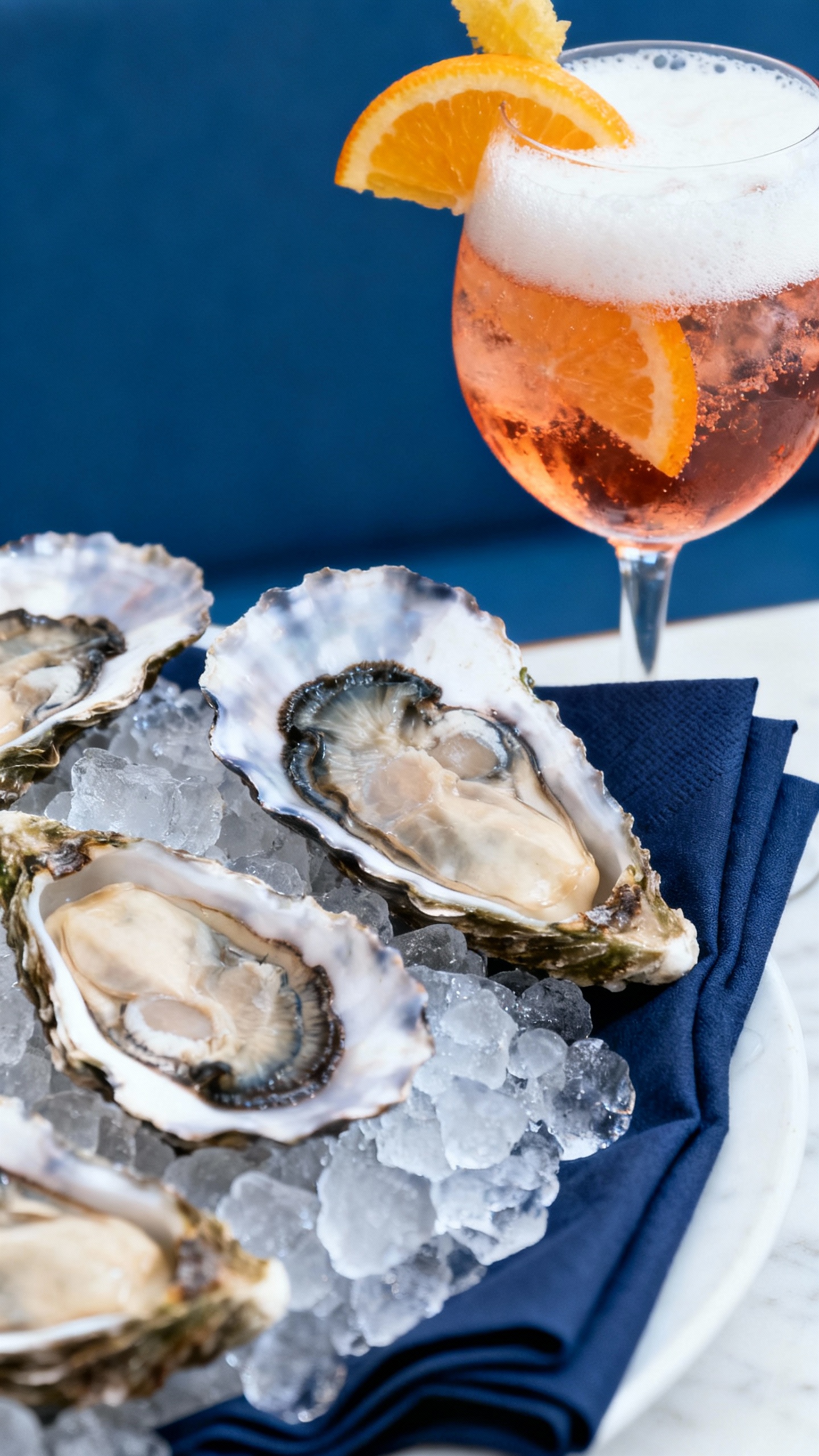 Closeup of oysters on ice, spritz cocktails, navy napkins